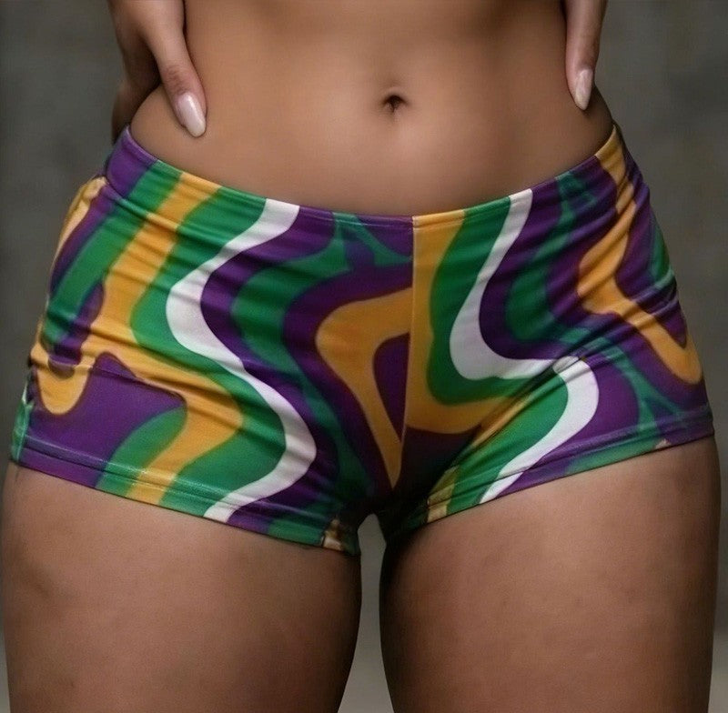 Colorful MARDI GRAS patterned shorts worn by a person on a neutral background