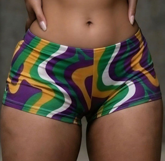 Colorful MARDI GRAS patterned shorts worn by a person on a neutral background